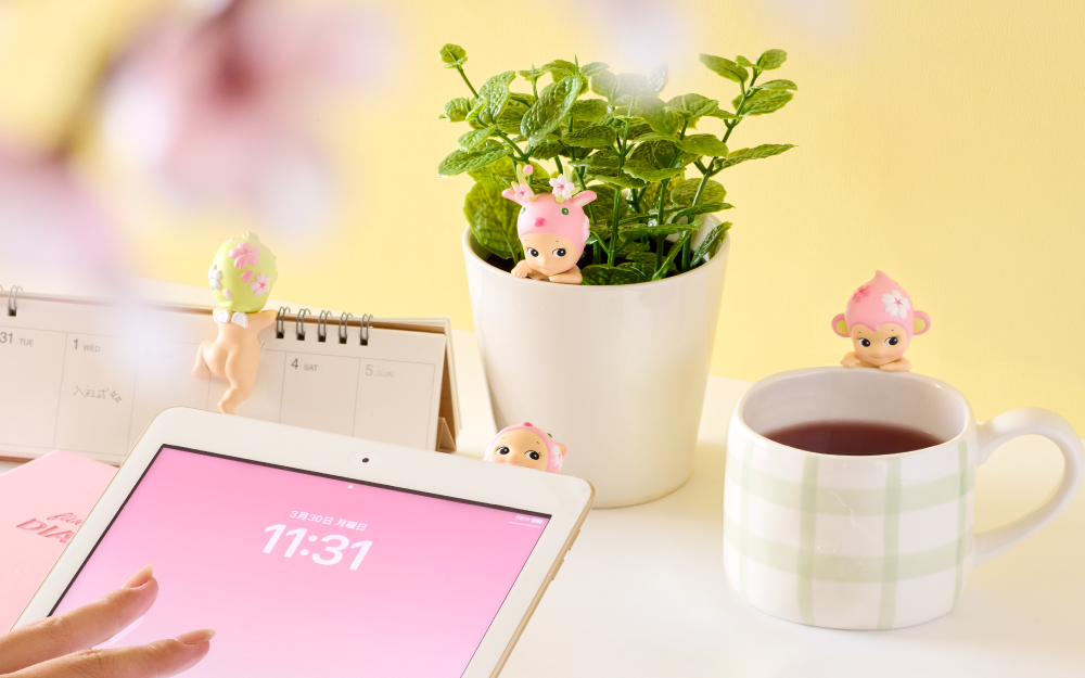 Cherry Blossom HIPPERS product image shows a tablet with a pink background and the Cat HIPPER peeking over the edge, a calendar with the Duck HIPPER facing away, a potted mint plant with the Reindeer looking out, and a white mug with the Monkey HIPPER watching over the contents